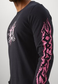 Schwarzes Langarm-T-Shirt mit einem auffälligen pinken Grafikdesign auf der Vorderseite und entlang des linken Ärmels, aus weichem Baumwollmaterial gefertigt.