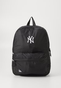 Zaino in nylon nero con una tasca frontale con zip, caratterizzato da un logo e testi bianchi dei New York Yankees. Texture liscia, forma standard, spallacci regolabili.