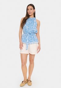 Haut sans manches bleu clair avec un motif texturé, taille cintrée et détail à nouer, associé à un short crème et des chaussures en osier.