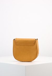 Borsa a spalla in pelle gialla con una texture liscia, forma arrotondata e chiusura a patta. Presenta cuciture minime e un design pulito.