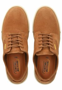 Zapatillas de ante marrón con un acabado texturizado, que cuentan con un diseño de cordones, una suela de goma beige y un acento de logo amarillo en el lateral.