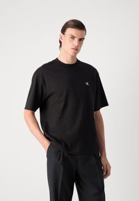 T-shirt nera a maniche corte realizzata in cotone, con scollatura rotonda e un piccolo logo bianco sul lato sinistro del petto. Texture liscia e vestibilità rilassata.