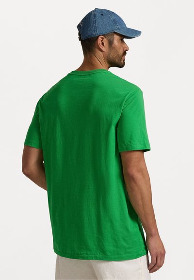 Zaļš kokvilnas T-kreklis ar apaļu kakla izgriezumu un īsām piedurknēm, skatoties no mugurpuses. Audumam ir maiga, gluda tekstūra.