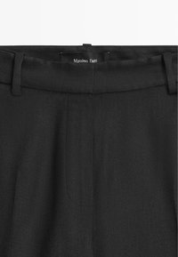 Schwarze, maßgeschneiderte Hose mit Gürtelösen, verdecktem Frontverschluss und sichtbarem "Massimo Dutti"-Etikett im Inneren des Bunds.