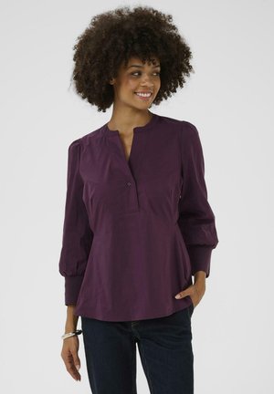 Lila Bluse mit Kragenloser Gestaltung, dreiviertellangen Puffärmeln und gerafften Details. Hergestellt aus leichtem Stoff mit glatter Textur.