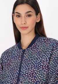 Jachetă bomber albastră cu un model geometric în diverse culori. Dispune de închidere cu fermoar și guler și manșete ribbed. Textură netedă.