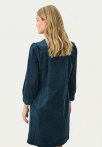 Wollkleid in tiefem Marineblau, mit langen Ballonärmeln und gerader Silhouette sowie einer strukturierten Ripp-Oberfläche.