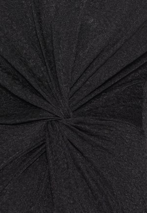 Tissu noir texturé noué au centre, créant des plis rayonnants et un effet froncé.