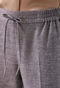 Grijze houndstooth broek met een elastische tailleband en trekkoord. Het materiaal lijkt zacht met een gestructureerde afwerking.