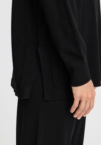 Pulover negru din tricot, cu o croială lejeră, slituri laterale la margine și manșete ribbate. Textură moale și design minimalist.