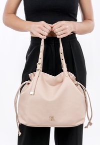 Light pink leather handbag with a cinched top, gold hardware, and two adjustable straps; features a logo on the front.