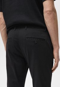 Crne hlače slim fit kroja, s glatkom teksturom, gumbom na stražnjim džepovima i petljama za remen na struku.