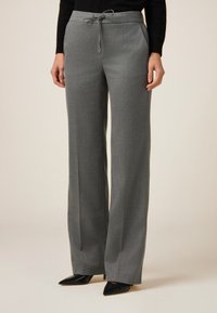 Pantalones de pierna ancha grises con cintura elástica y bolsillos laterales, confeccionados en una tela suave y texturada. Combinados con tacones de punta negros.