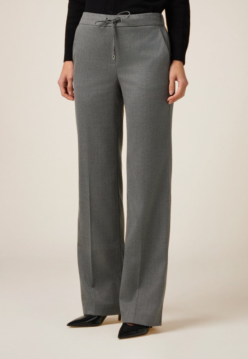 Pantalones de pierna ancha grises con cintura elástica y bolsillos laterales, confeccionados en una tela suave y texturada. Combinados con tacones de punta negros.