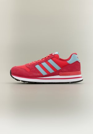 Czerwony sneaker Adidas z jasnoniebieskimi paskami i akcentami, biała podeszwa środkowa, czarna podeszwa zewnętrzna, pokazany z profilu na neutralnym tle.