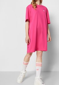 Rosa oversized t-shirt klänning med korta ärmar, sidofickor och vit logotyp. Matchas med vita strumpor och sneakers med rosa detaljer.