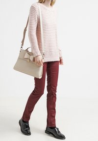 Beige handväska med rosettdetalj, texturerad yta; ljusrosa stickad tröja; vinröda skinny jeans; svarta skor med spänne.