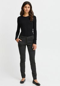 Top nero a maniche lunghe abbinato a pantaloni grigi scuri sartoriali. I pantaloni presentano una texture liscia e tasche laterali, completati da ballerine nere.