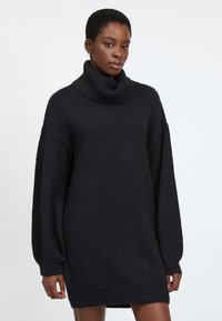 Schwarzes, übergroßes Strickkleid aus strukturiertem Maschenstoff, mit einem Rollkragen und langen, luftigen Ärmeln mit gerippten Manschetten.