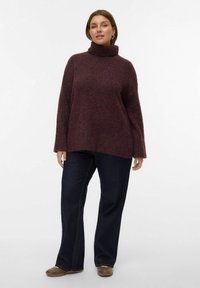 Pull à col roulé bordeaux avec une coupe ample, présentant une texture côtelée et des épaules tombantes, associé à un jean foncé évasé.
