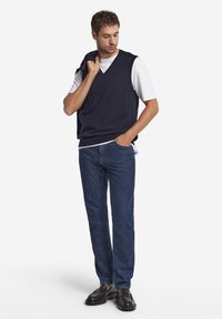 Marinblå stickad väst över en vit t-shirt, kombinerad med mörkblå jeans och svarta loafers. Enkel design med V-ringning och avslappnad passform.