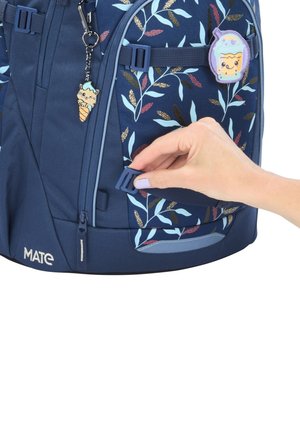 Hand with purple nail polish adjusting strap on blue floral-patterned school backpack with cartoon patch and keychain.