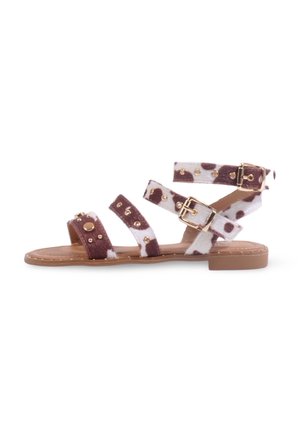 Sandales en cuir de vachette marron et blanc avec plusieurs brides qui se chevauchent, accents en métal doré et semelle plate. Dessus texturé avec des clous.