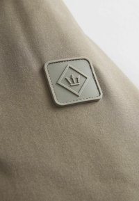Bežna tkanina mekanog tekstura, sa kvadratnim sivoj zakrpi urezanom sa dizajnom krune i dijamanta, ušivenom svijetlom koncem.