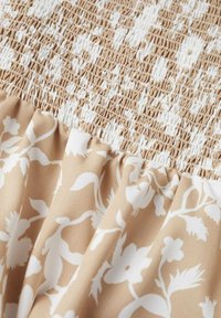 Tissu beige avec des motifs floraux blancs en bas et un design froncé texturé en haut, présentant une apparence douce et plissée.
