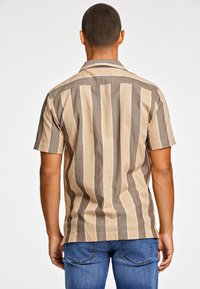 Camisa de manga corta con rayas verticales en tonos beige y marrón, con una textura suave y un diseño de cuello relajado.