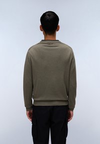 Olivgrüner Sweatshirt, Baumwollmischung, Rundhalsausschnitt, gerippte Bündchen, der Rücken ist mit einem kleinen Logodetail versehen. Kombiniert mit schwarzen Cargo-Hosen.