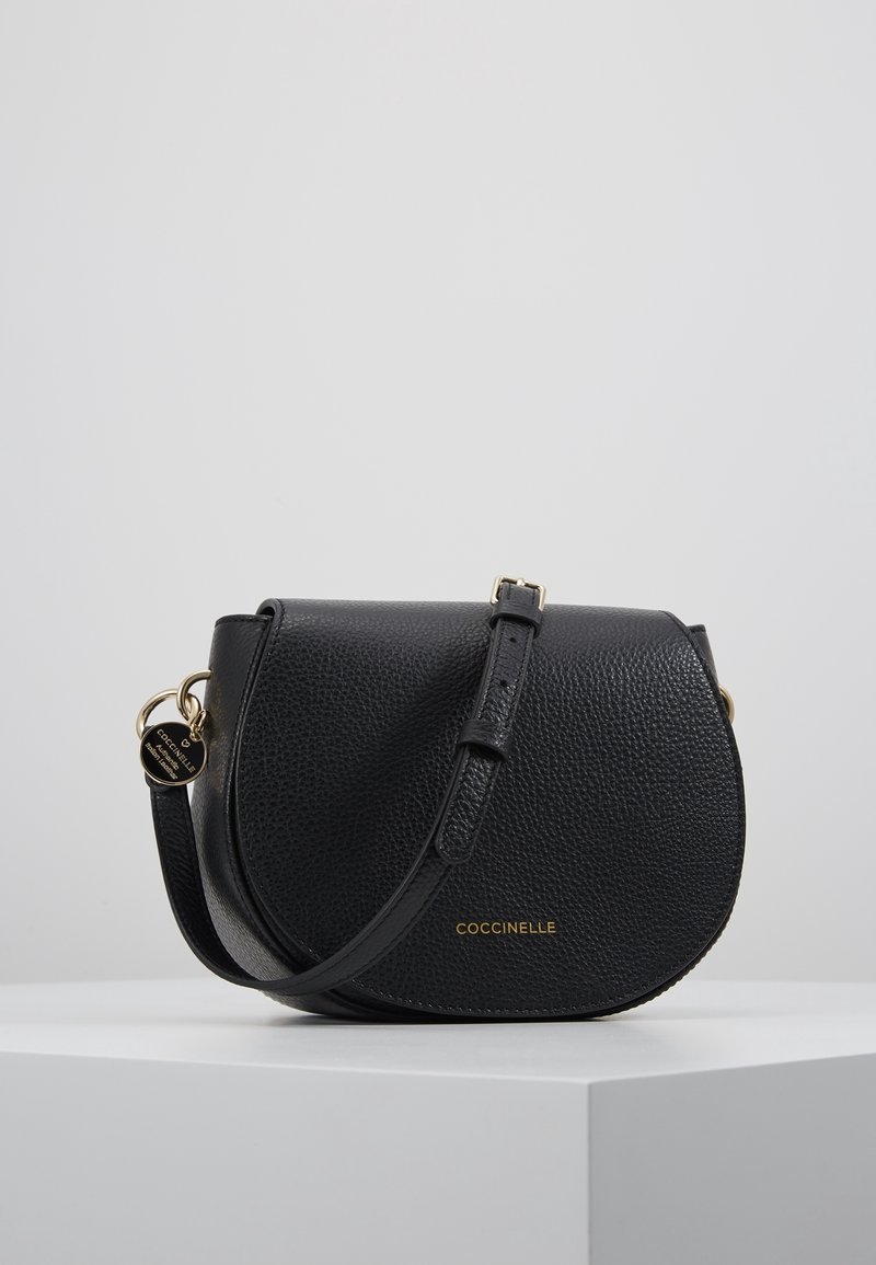 Borsa a tracolla in pelle nera con texture, flap curvo, tracolla regolabile, accessori in tonalità oro e marchio "COCCINELLE" sul davanti.