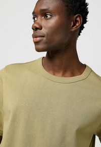 T-shirt in cotone verde oliva con colletto a giro e maniche corte, con una texture liscia e un design minimalista. Nessun motivo o grafica.