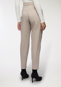 Beżowe spodnie w kant o prostym kroju, gładkiej teksturze i dwóch tylni pockets, zestawione z czarnymi botkami na obcasie.
