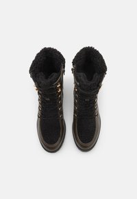 Bottes en fourrure noire, avec une tige texturée, dotées de quincaillerie métallique dorée, d'un design à lacets et d'une pointe en cuir lisse.