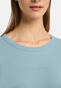 Tricou din bumbac de culoare bleu deschis cu guler rotund și logo-ul embosat "ELBSAND" pe față. Textură netedă și design ajustat.