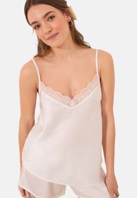 Camisole en soie blanche avec des bretelles spaghetti ajustables, présentant une bordure en dentelle découpée le long de l'encolure et une coupe fluide et lisse.