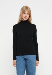 Maglia nera a maniche lunghe con collo alto realizzata in tessuto morbido, caratterizzata da un design aderente e una texture liscia. Abbinata a jeans azzurri a vestibilità ampia.
