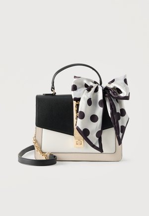Crna, bijela i bež torba sa zlatnim kopčom i lancem, ukrašena velikom bijelom svilenom mašnom s crnim točkicama na ručki.