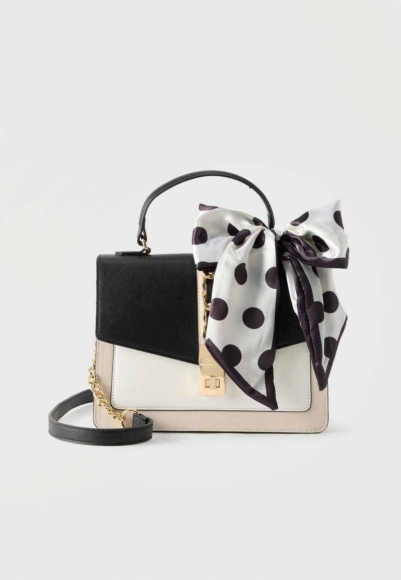 Sac à main noir, blanc et beige avec fermoir en or et chaîne, décoré d'un grand nœud en soie blanc à pois noirs sur la poignée.