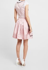 Abito dirndl in satin rosa con intricati accenti di pizzo bianco, gonna plissettata e corpino aderente. Presenta una schiena texturizzata e maniche in pizzo bianco.