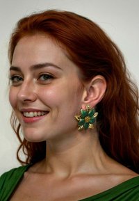 Green floral earrings featuring a gold base and textured green petals, accented with a central gold flower, worn by a model with red hair.