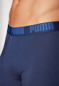 Marinblå boxerkalsonger med ett tjockt midjeband som har "PUMA"-logotypen i fet stil. Slät textur med en figurnära passform och synlig sömnad.