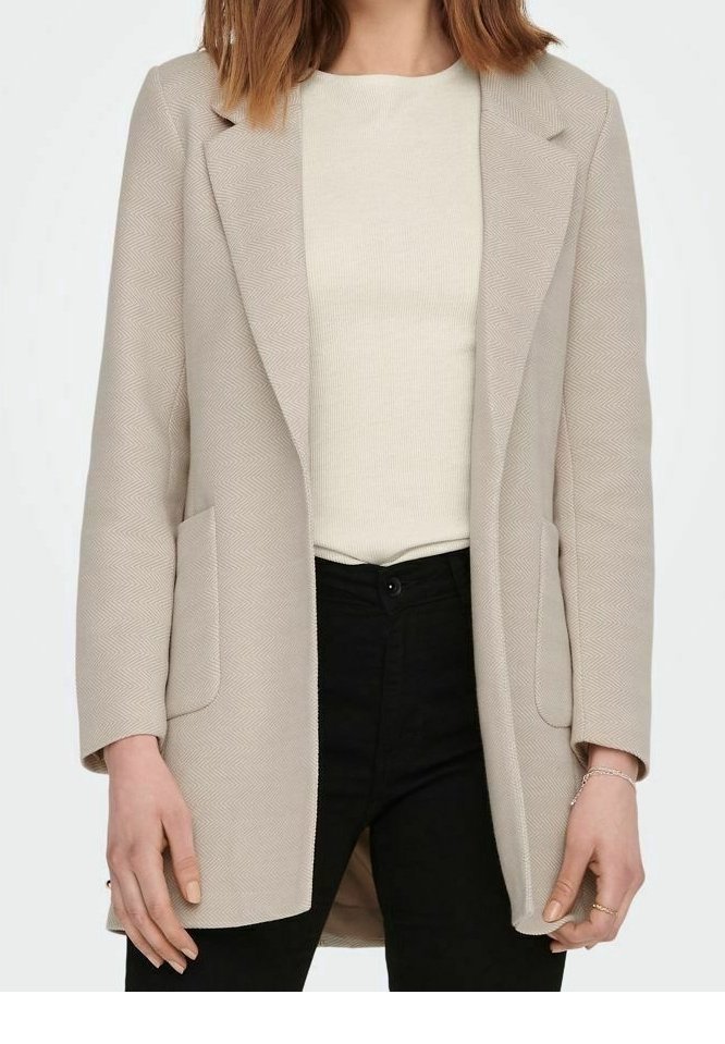Beige blazer s rybí kostrou se dvěma předními kapsami, propracovaný design, strukturované klopy, nošený přes světlobéžový top a černé kalhoty.