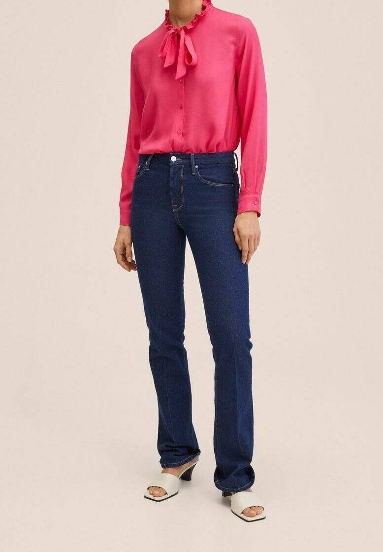 Blouse fuchsia avec col à volants, jean évasé en denim bleu, et mules blanches à bout ouvert. Tissu lisse et lignes épurées visibles.