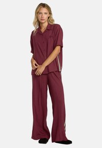 Set di abbigliamento da lounge bordeaux composto da una camicia a maniche corte con bottoni e pantaloni a gamba larga con dettagli a strisce verdi e bianche. Tessuto morbido e leggero.