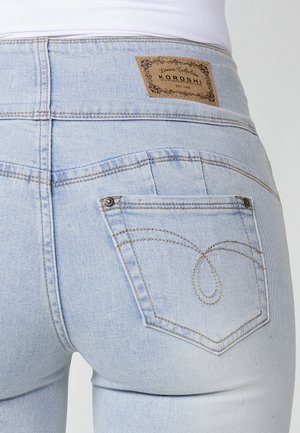 Jeans de mezclilla azul claro con cintura alta, que presentan una etiqueta de cuero con la palabra "KOROSHI" y costuras decorativas en los bolsillos traseros.