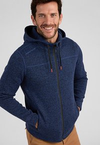 Navyblaues Zip-Hoodie aus strukturiertem Fleece, mit Kapuze, schwarzem Reißverschluss und orangen Zugbandakzenten. Schlanker Schnitt mit seitlichen Taschen.