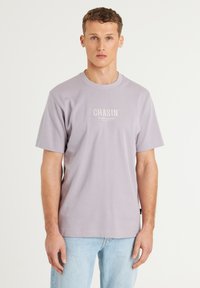 T-shirt cotone lavanda con collo rotondo e maniche corte, con il logo bianco "CHASIN'" stampato sul davanti. Vestibilità classica.