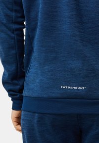 Laivastonsininen teksturoitu huppari ja vastaavat housut, joissa on "Sweidemount"-logo lähellä alaosan takahelmaa.